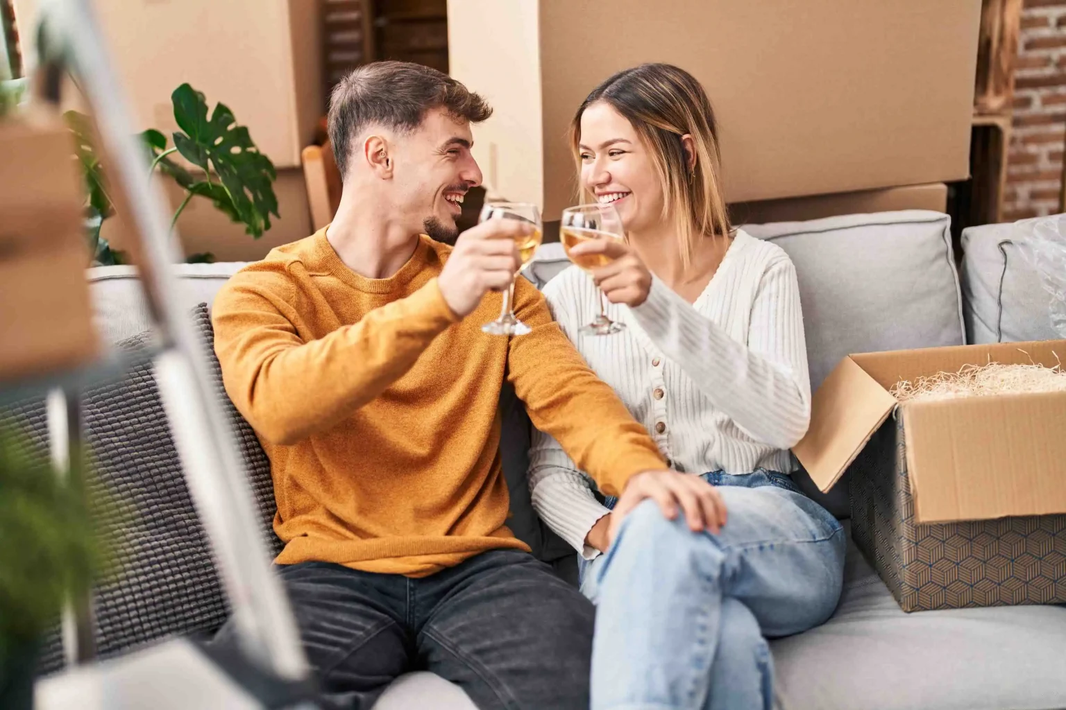 Young couple toasting wine on sofa in new home interior